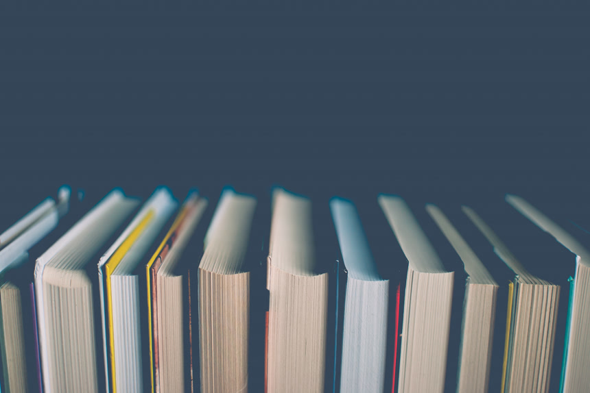 黑色背景前的一排五颜六色的书特写     知识、教育、学习和文学的抽象概念