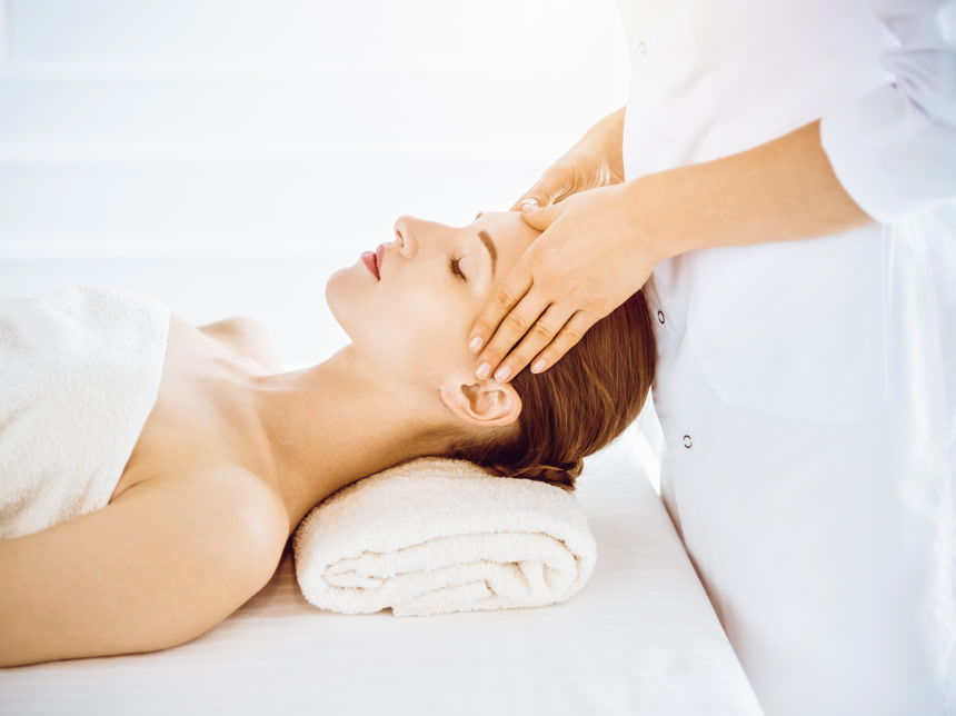 在阳光普照的温泉中心，漂亮的女人正享受着闭上眼睛的面部按摩美容美体