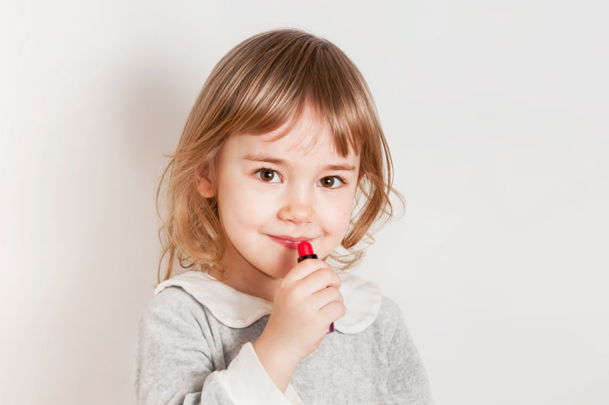 小女孩用口红涂嘴唇.在白色背景前照片 