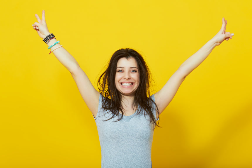 站在黄色背景前双手举起比耶的长发外国女子大笑人像照片