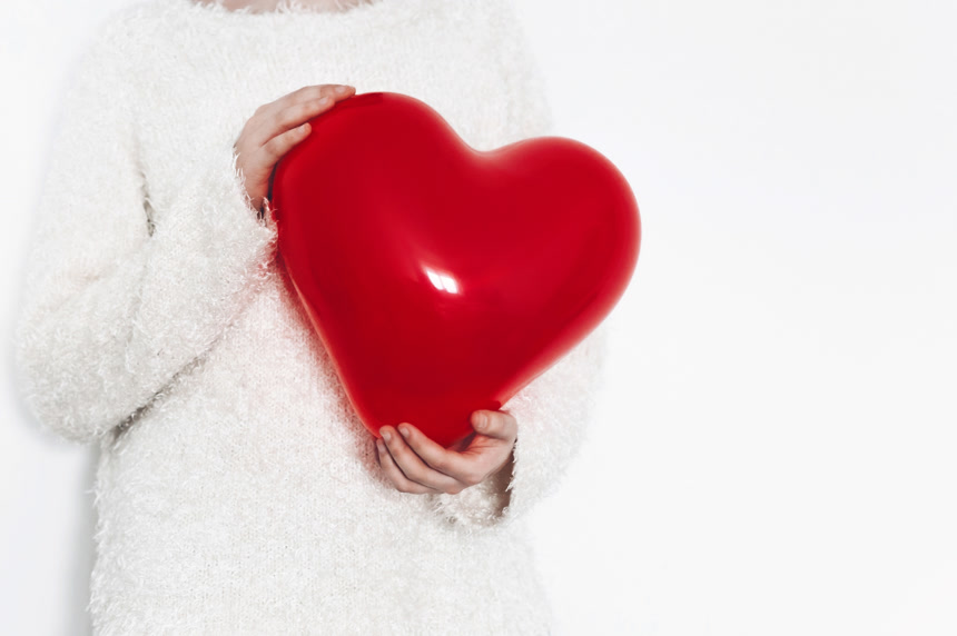 白色背景上穿着白色毛衣的女人手捧红色心形气球影棚摄影