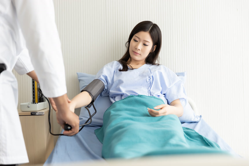 医生检查躺在医院病床上的亚洲妇女的血压医疗保健