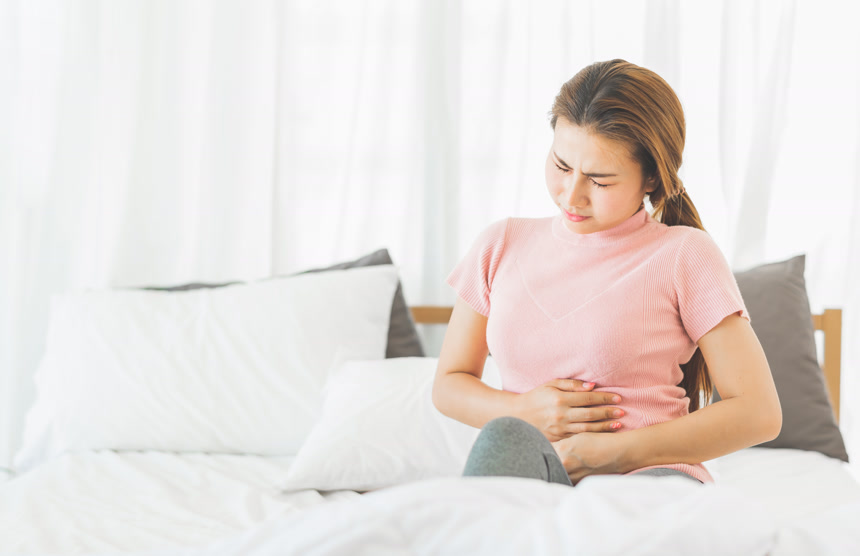 亚洲年轻女子坐在床上表情痛苦的抱着肚子医疗健康