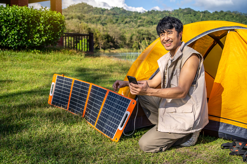 年轻的旅行者放松露营便携式太阳能电池板，用多功能电缆充电智能手机，露营或家中没有电的清洁能源