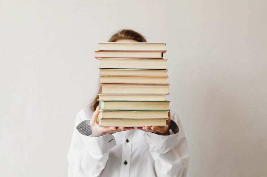 女生双手举着一堆书挡着脸生活方式