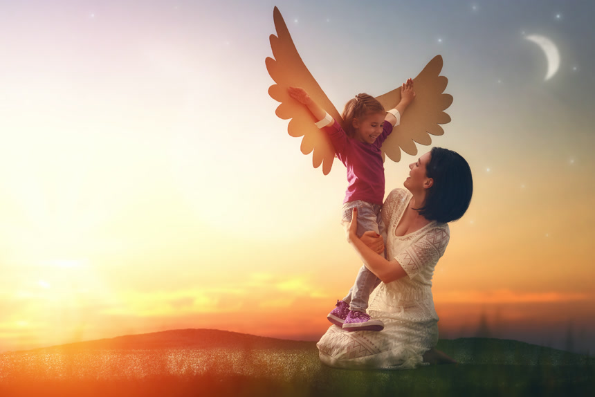 黄昏下抱着带着翅膀的小女孩的母亲家庭人像
