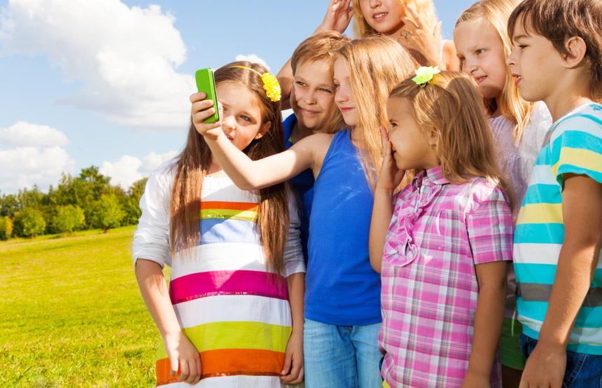 草地上小女孩用手机与朋友们自拍摄影图
