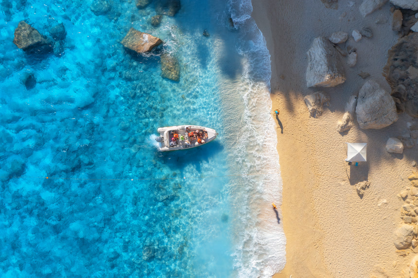 Aerial view of boat, sandy beach and blue sea with waves at sunset. Summer in Sardinia, Italy. Top drone view of motorboat, shore, stones in transparent water. Colorful tropical landscape. Travel海水船只自然景观
