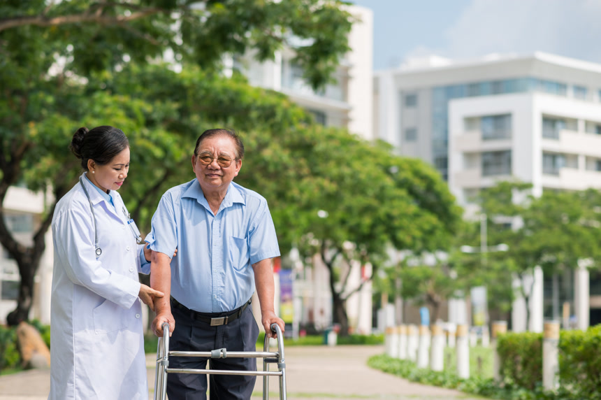 女医生帮助老年男病人行走在医院公园练习养老院康复治疗术后恢复