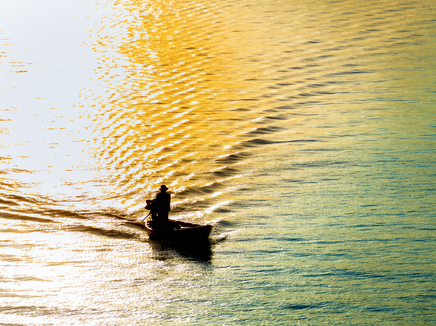 渔船在日落时穿越大海的在平静的海面上航行一个人在金色日落下乘船旅行