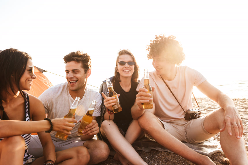海滩上喝啤酒聚会的四个年轻人   休闲生活概念