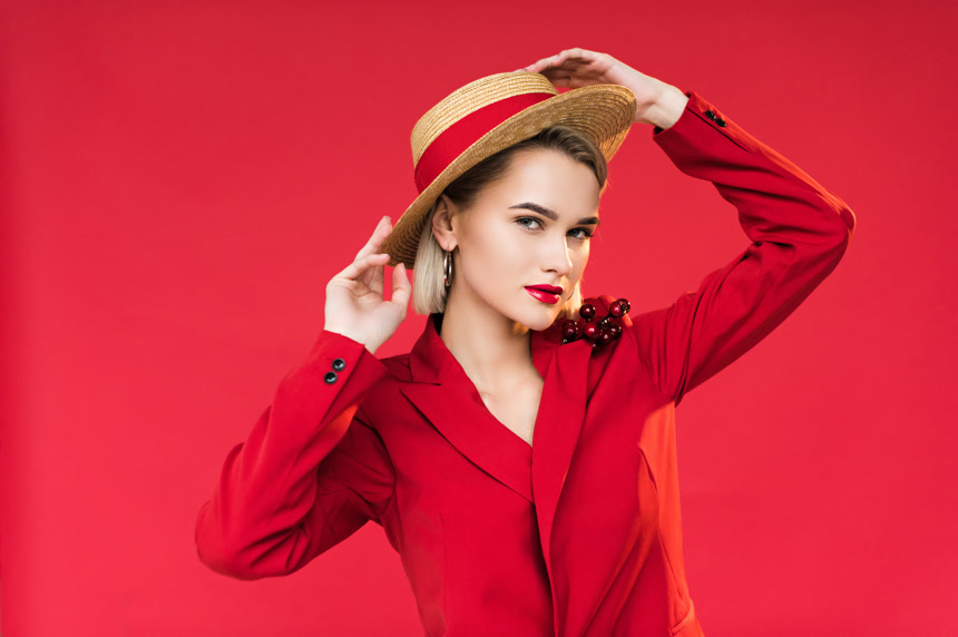 红色背景中时尚女孩手摸草帽的写真
