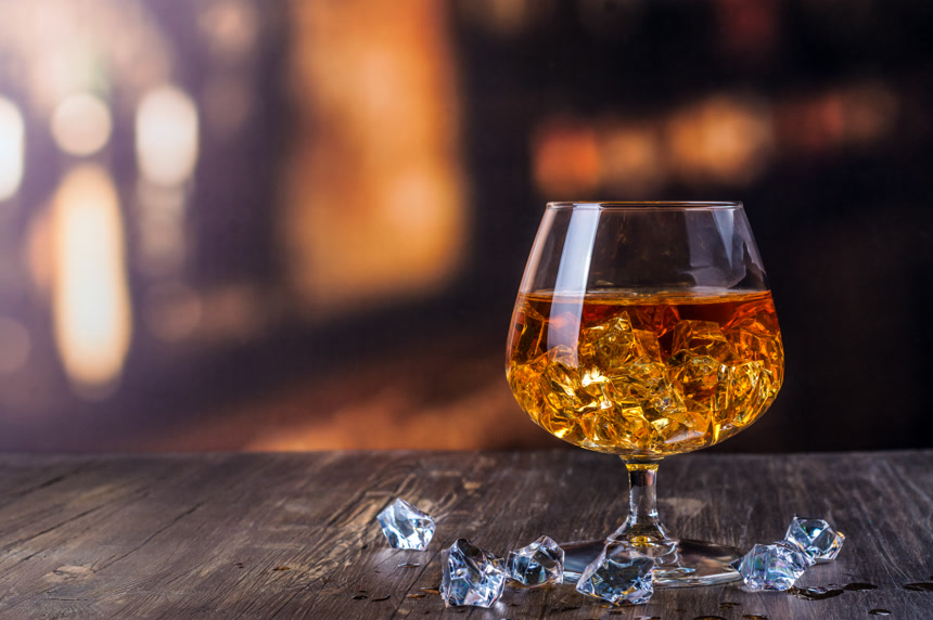 一杯金黄色的酒液在木质桌面上放置着，里面加了一些冰块