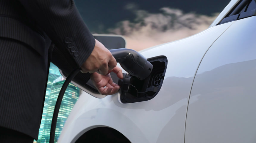 进步商人从充电站用充电器电缆插头给他的电动汽车充电城市背景.