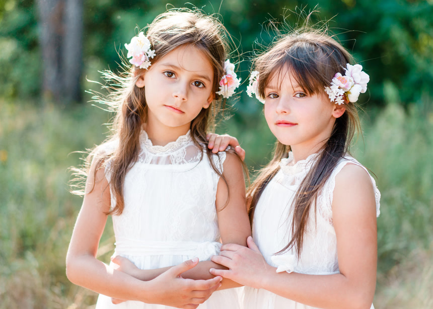 两位小女孩站在户外穿着白色的连衣裙头上都戴着花环