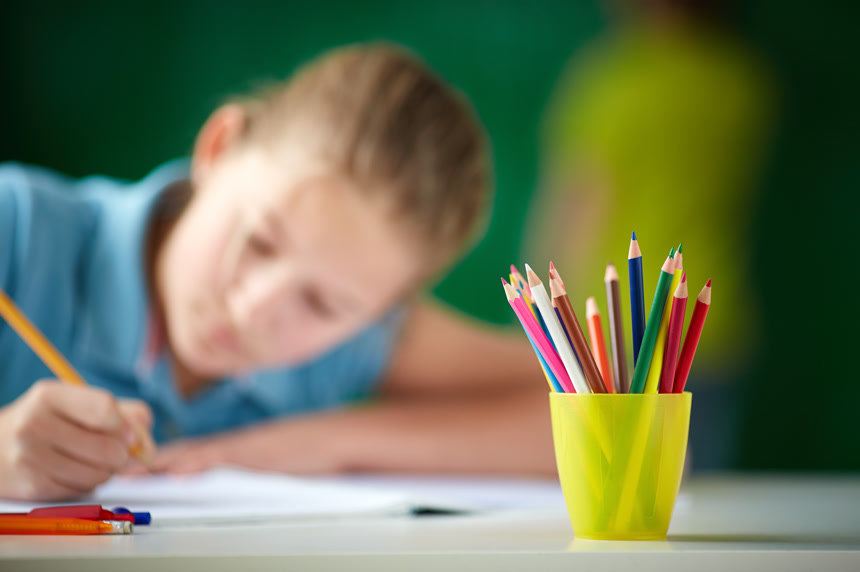 彩色绘画笔插在黄色笔筒里背景一个小女孩在认真的作画