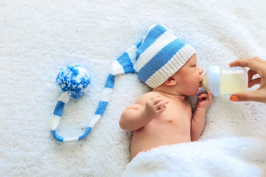 白人婴儿喝牛奶配方奶粉的侧视图而不知名的女性母亲拿着奶瓶 买正在喂食营养喂食