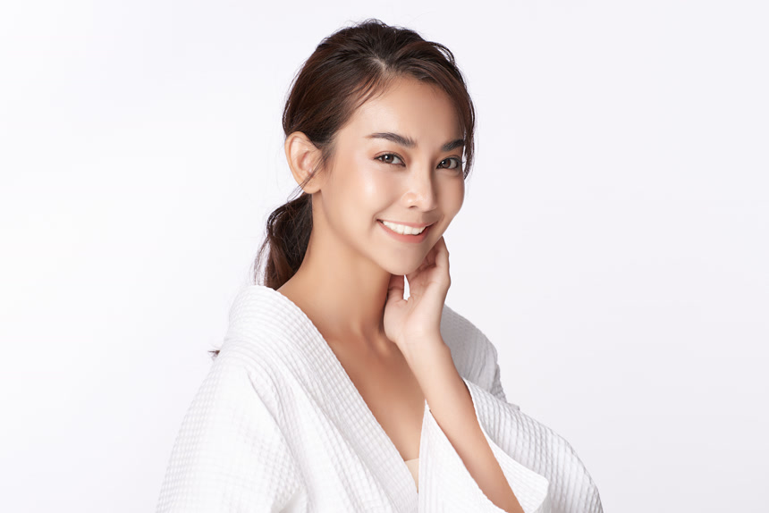 白色背景上年轻美丽的亚洲女人抚摸着自己的面部皮肤看着镜头微笑