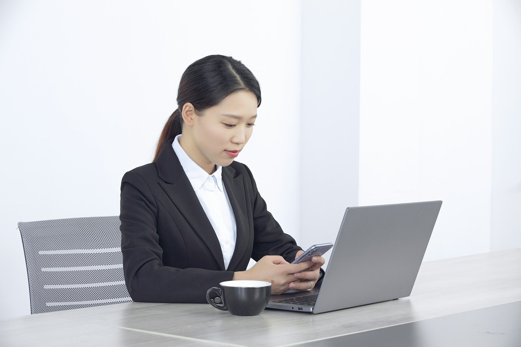 办公室电脑前看手机信息的商务女性图片