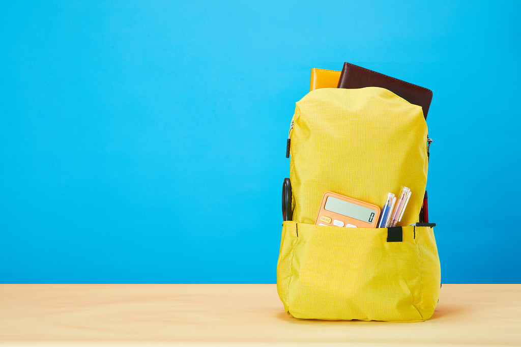 开学季蓝色背景上装满文具学习用品的黄色书包场景配图