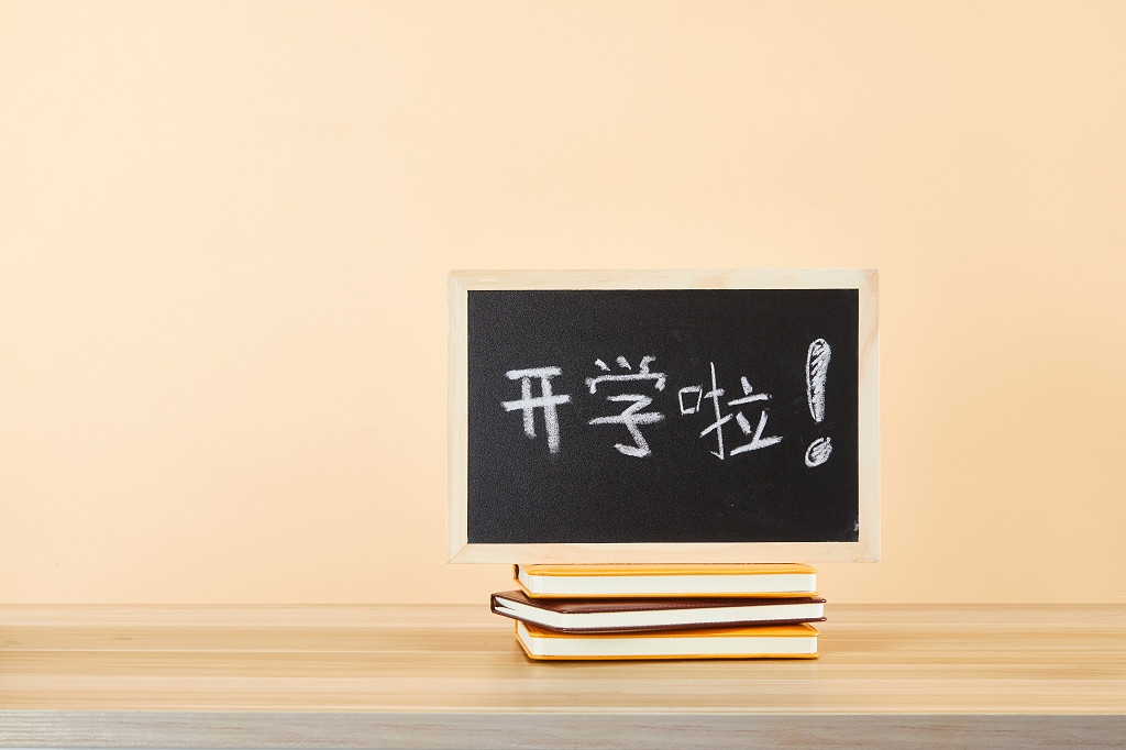 开学季写有开学啦的小黑板笔记本在课桌上的场景配图