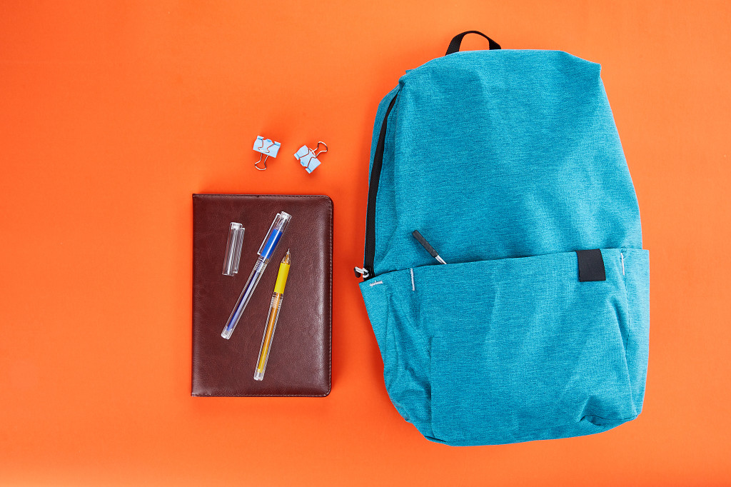 开学季蓝色书包笔记本文具在橙色背景上的场景配图俯视图