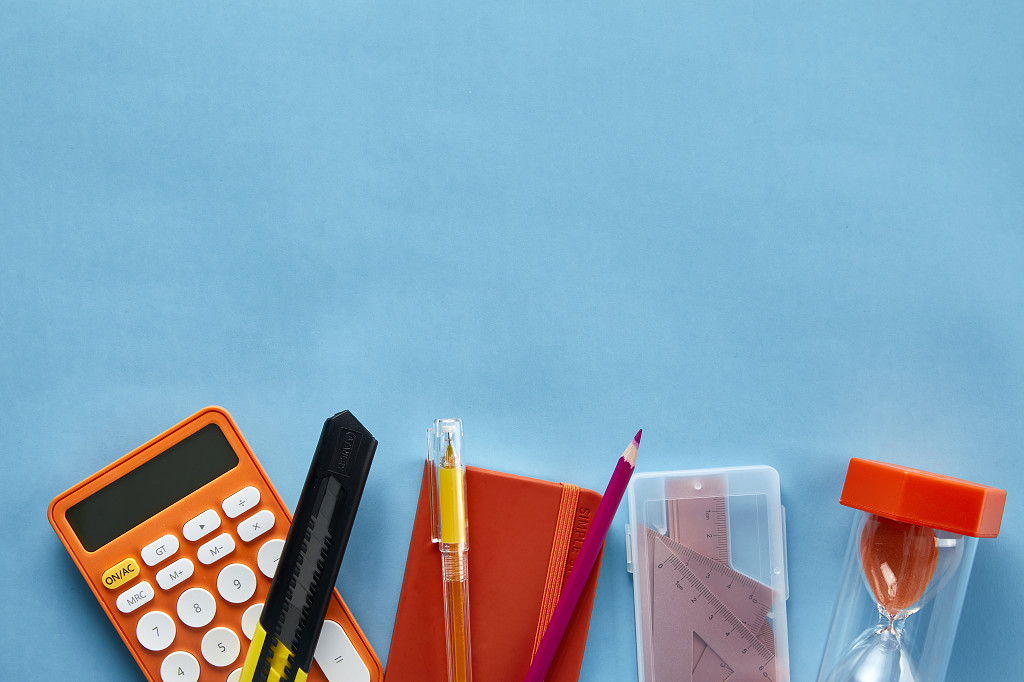 平铺在蓝色背景纸上的计算器笔记本沙漏文具学习用品场景教师节