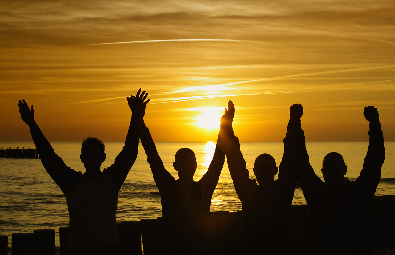 日落夕阳下在海边举起双手的四个人剪影奋斗奋斗奋斗精神努力