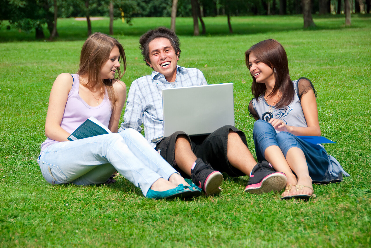 公园草坪上三个学生放松谈论欧美人物图