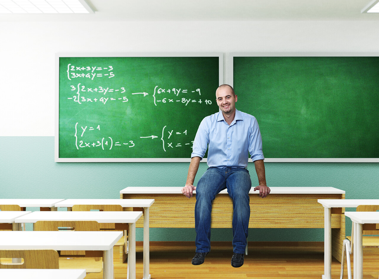 教室里白人教师坐在黑板前的课桌上