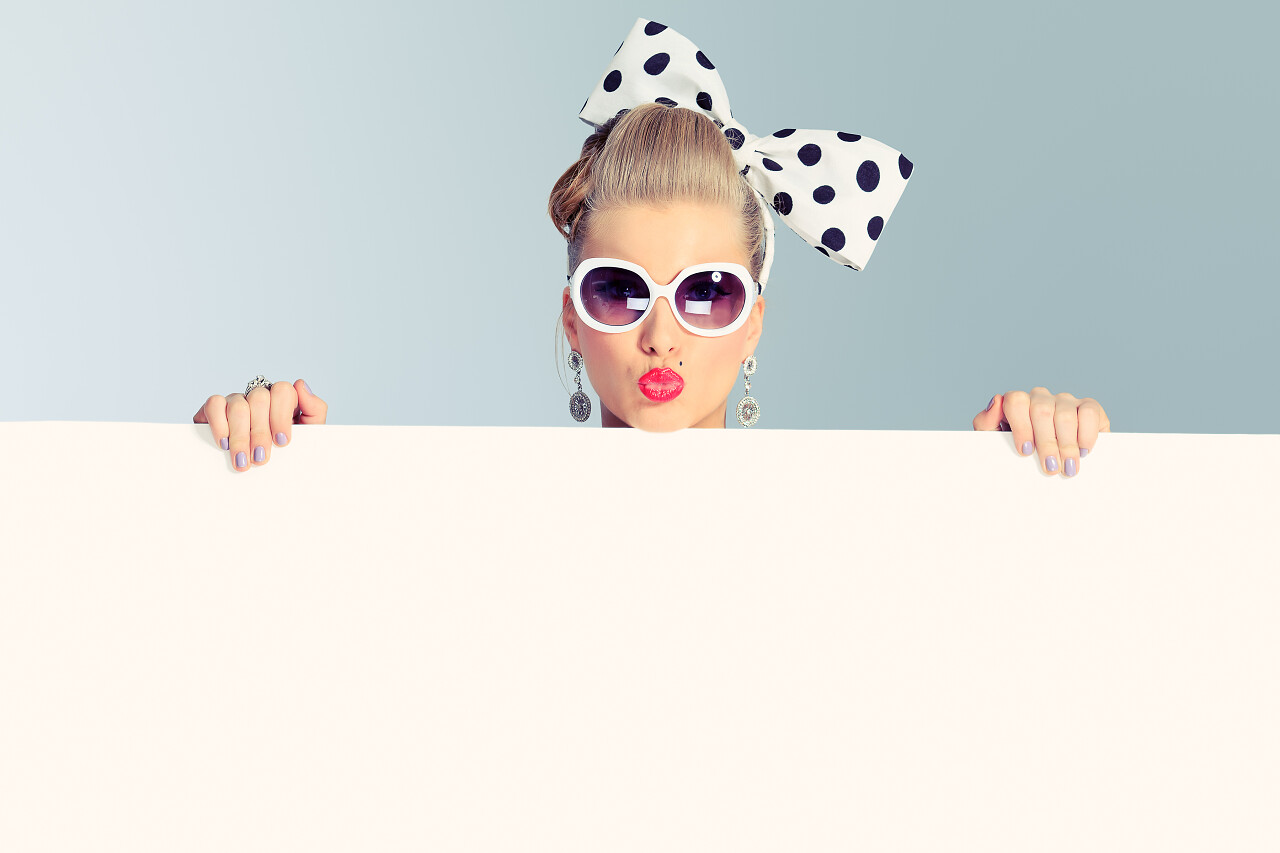 青灰色背景手拿反光板带着大蝴蝶结大墨镜美丽的年轻女子