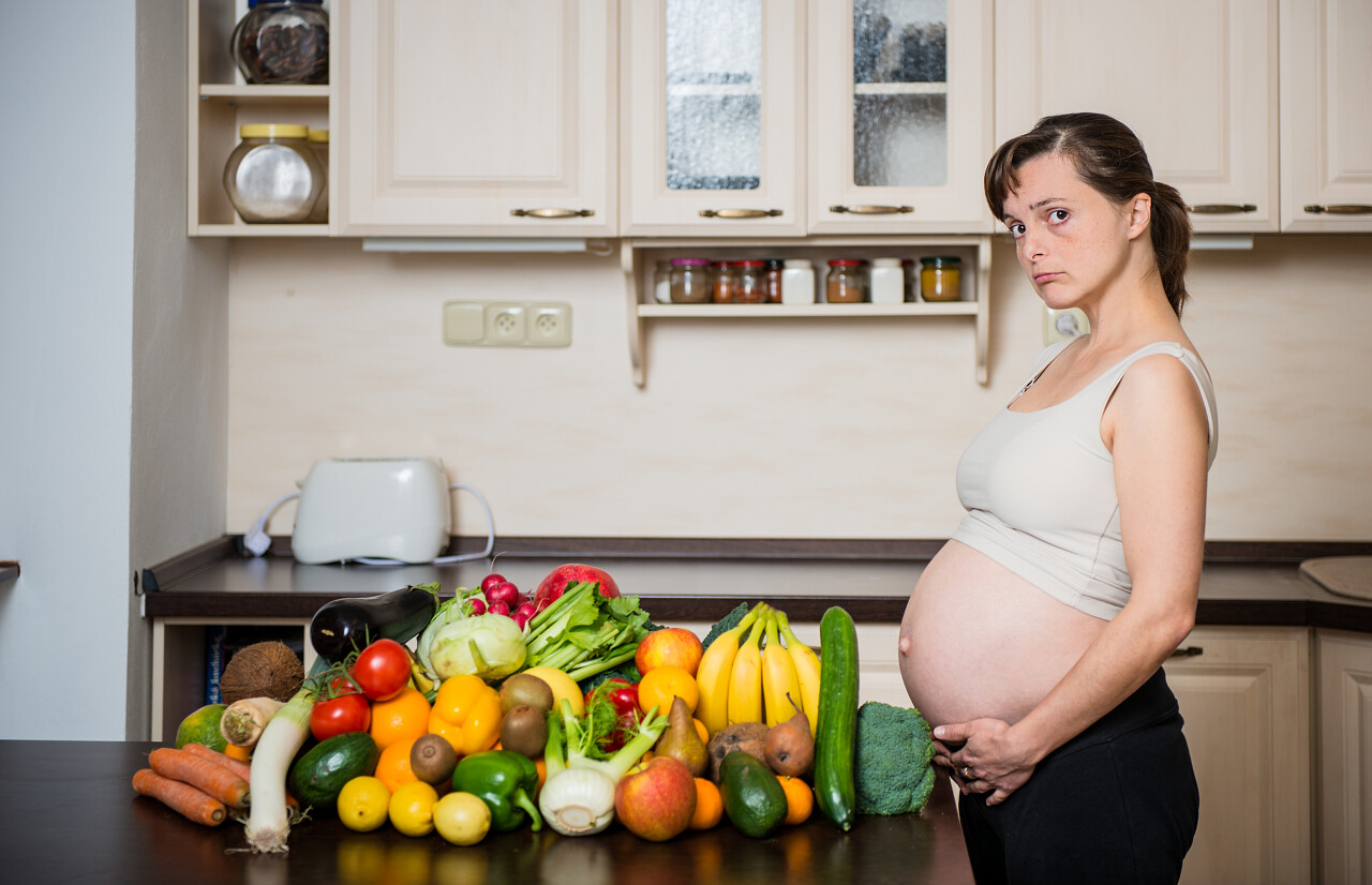 不开心的怀孕女人与丰富的蔬菜和水果中的厨房