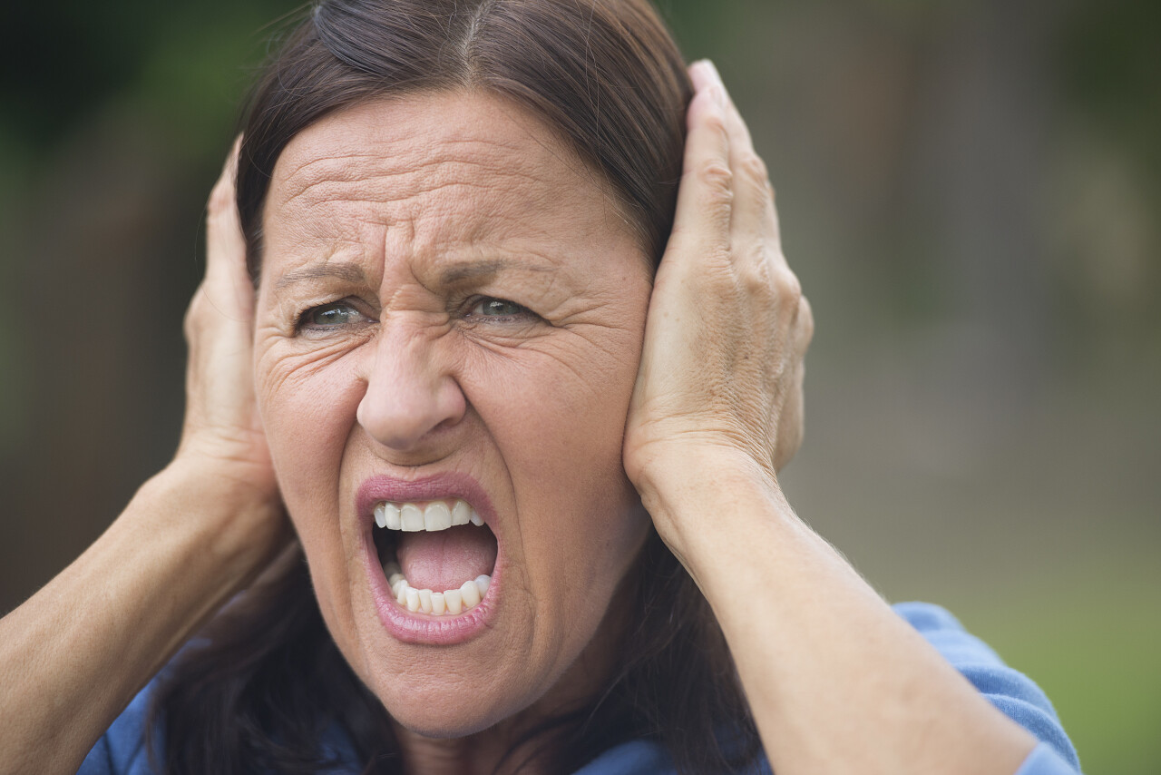 中年女子涵盖沮丧 愤怒或焦虑中用手强调她耳朵心烦孤立与室外背景模糊焦虑
