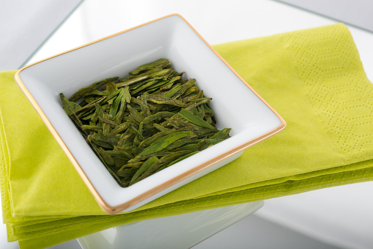 中国新鲜绿茶叶龙井的高质量在明亮的餐巾纸上的白色瓷碟上