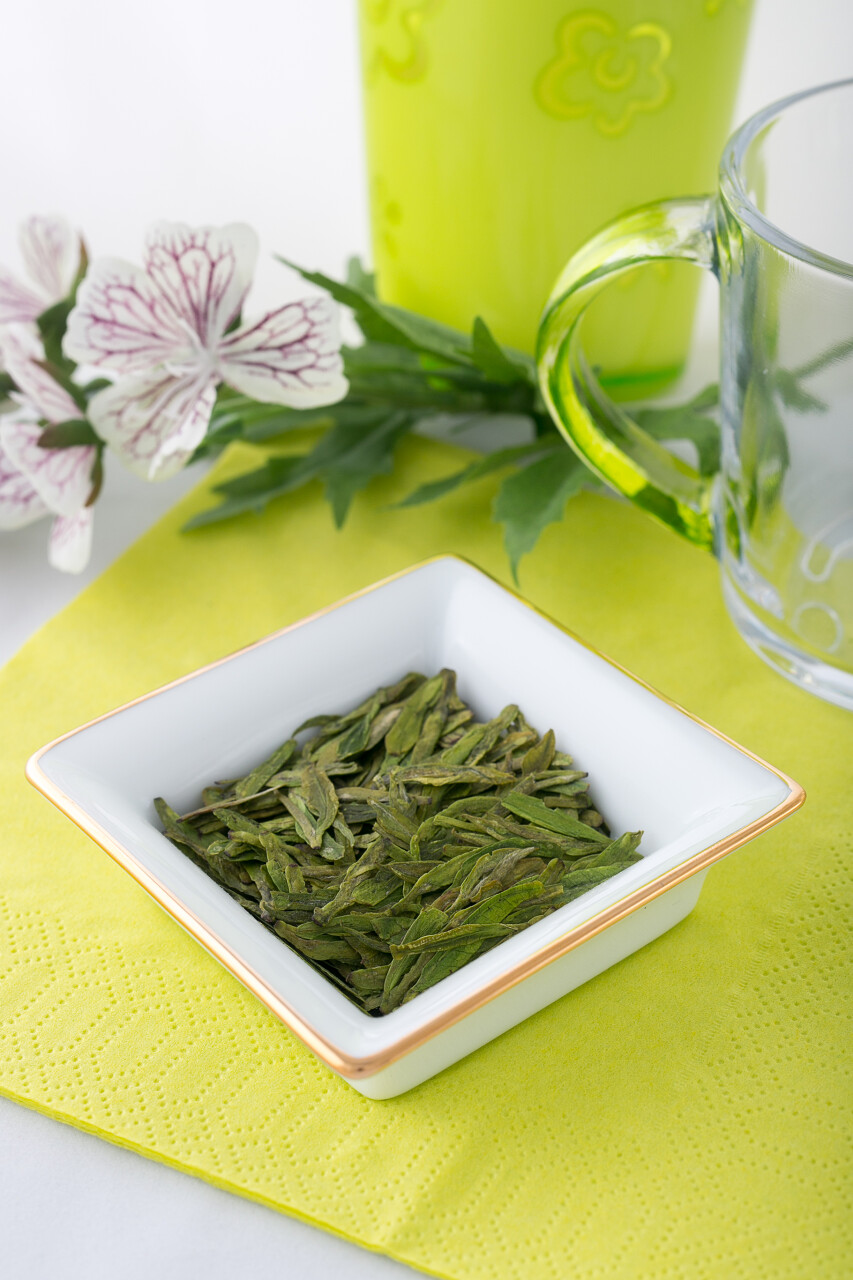 中国新鲜绿茶龙井的高质量在明亮的背景上的白色瓷碟有叶子花