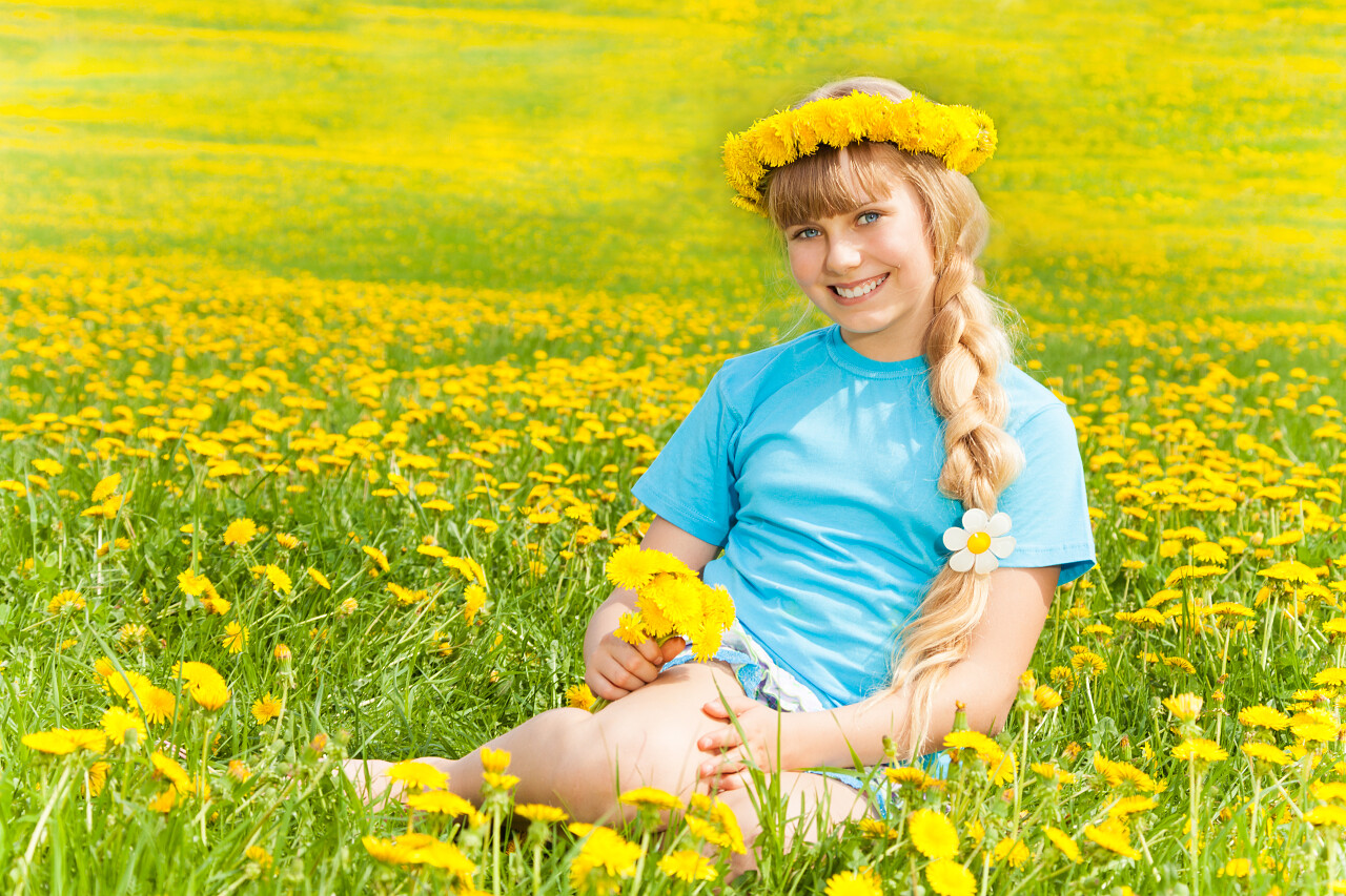 美丽金发女孩坐在黄色花丛中