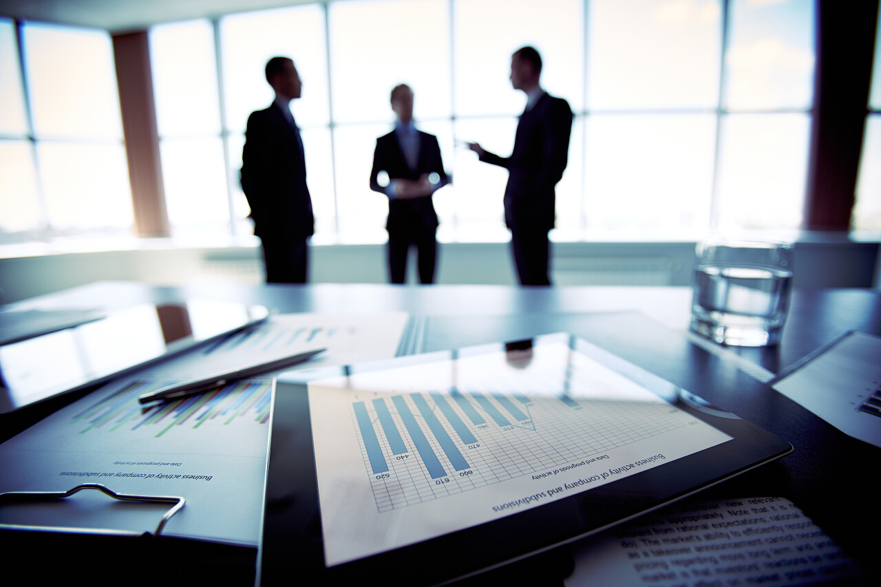 站在背景中的三个商人和显示财务数据的平板电脑特写