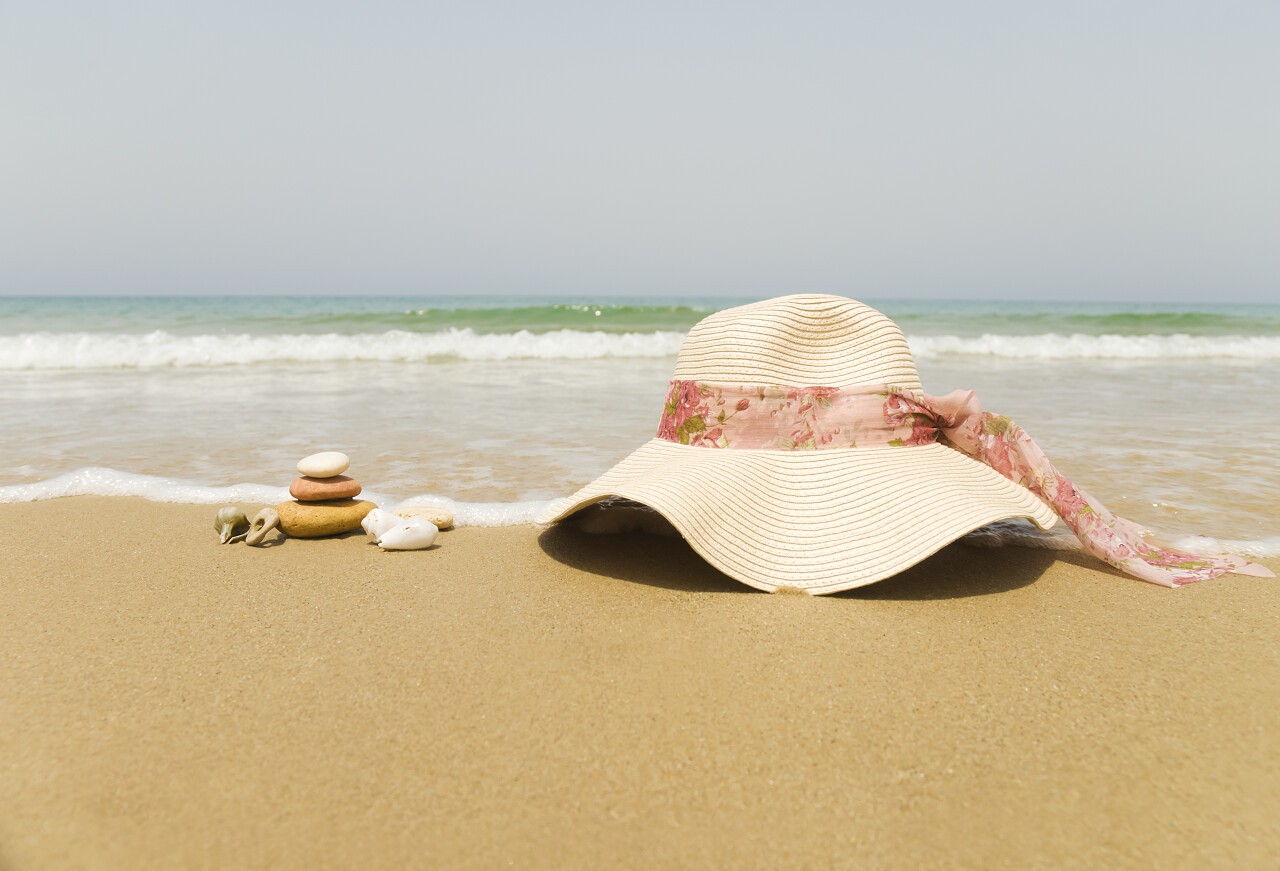 沙滩上一顶女性草帽编织帽与几块叠在一起的小石头