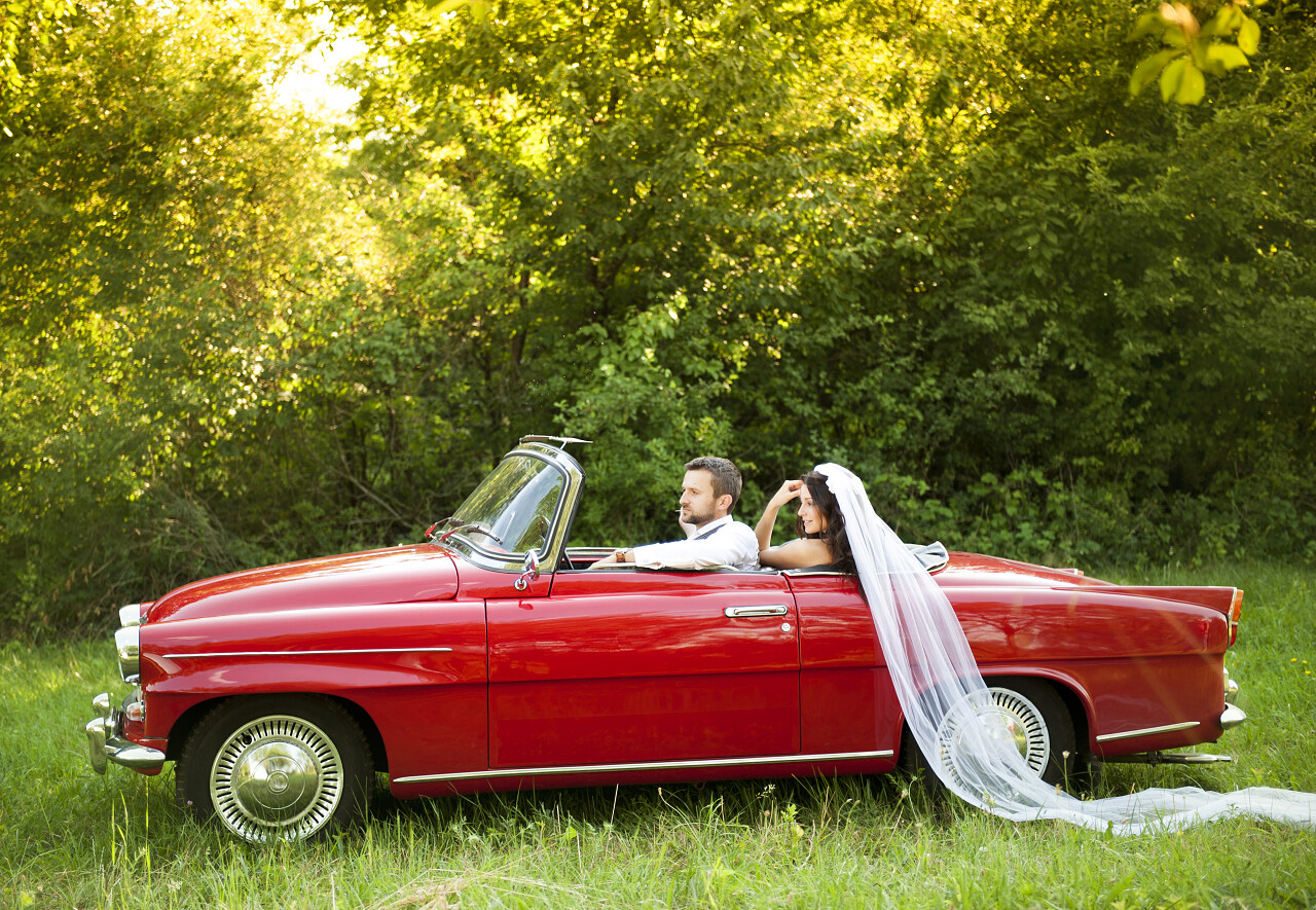 华丽的新娘和新郎在大自然中得到乐趣红色复古车
