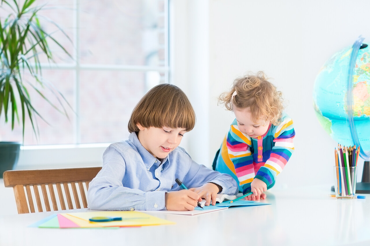 蹒跚学步的妹妹在桌子旁看小男孩做作业