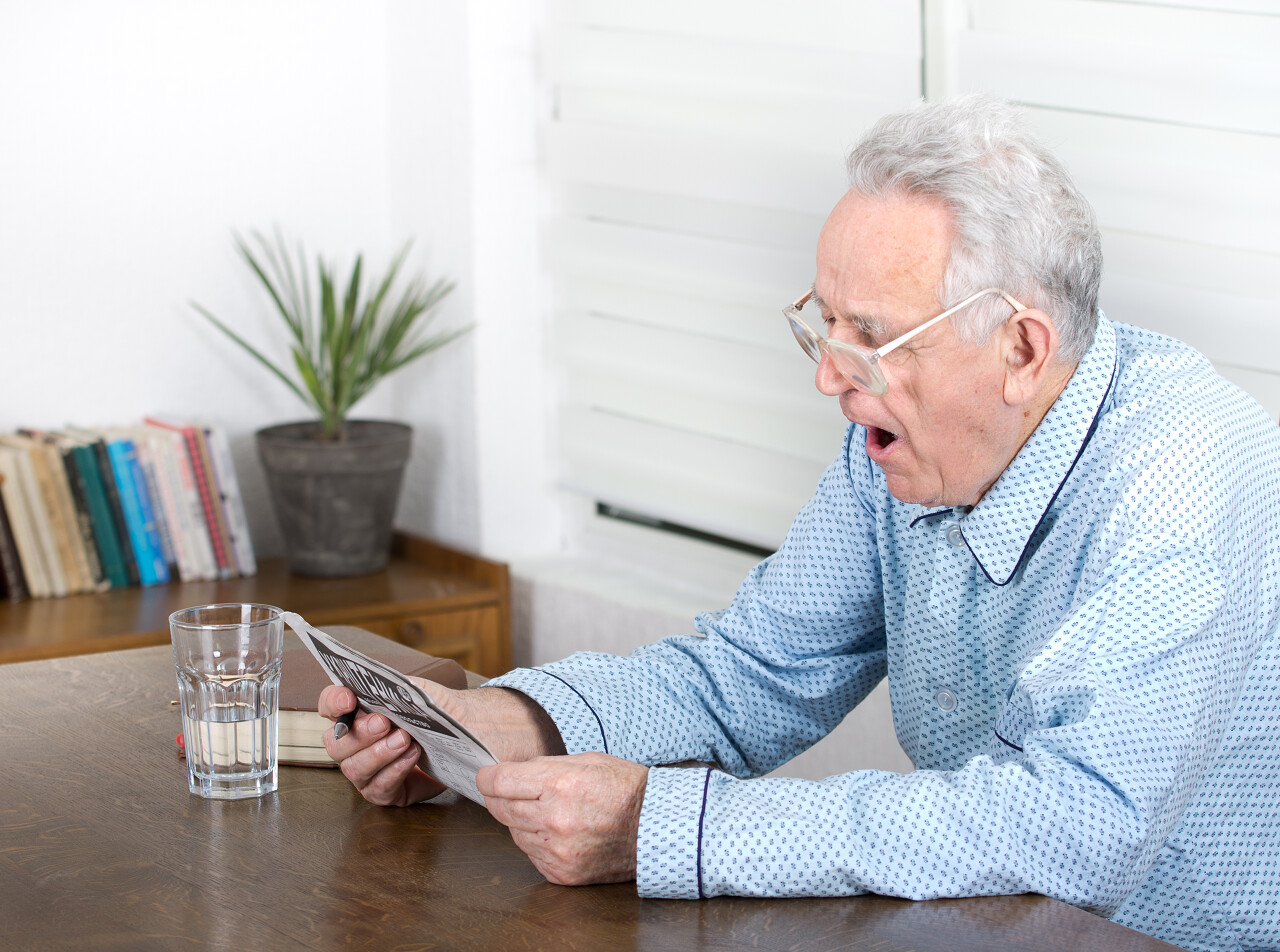 打呵欠时解决填字游戏的睡衣的老人