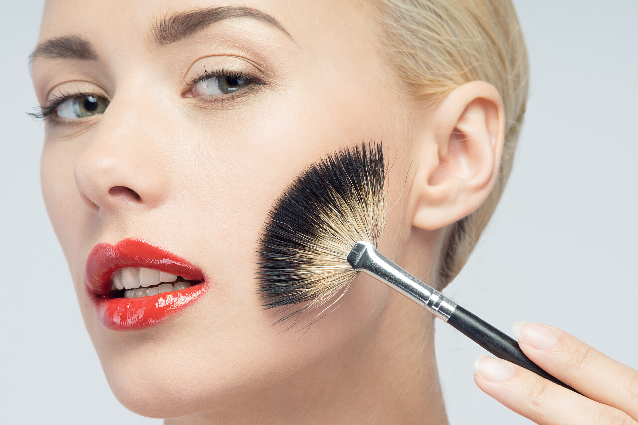 化妆用刷孤立的白色背景上的美丽年轻的金发女子的肖像