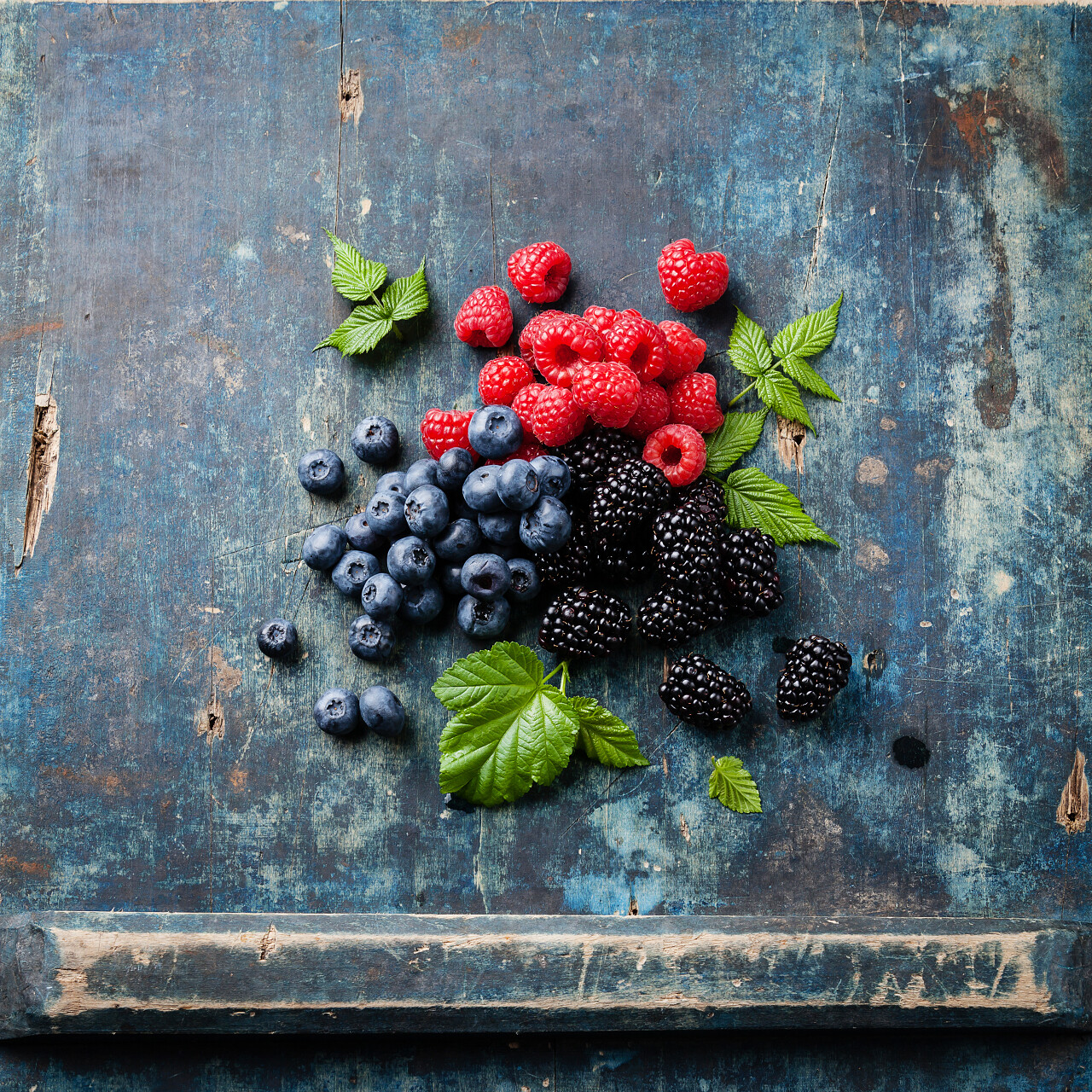 混合的新鲜的浆果并带蓝色木背景上的叶子
