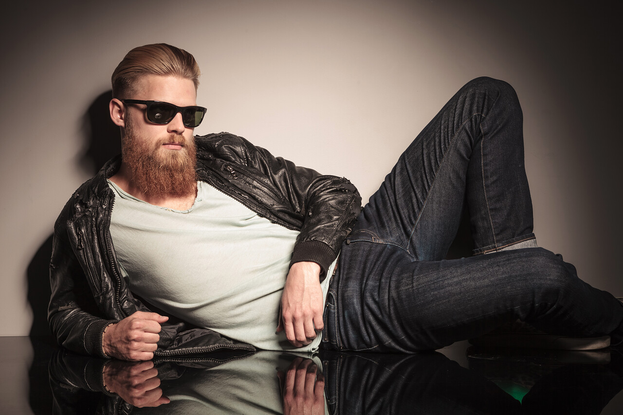 在皮夹克和太阳镜在地板上看着相机的男模特