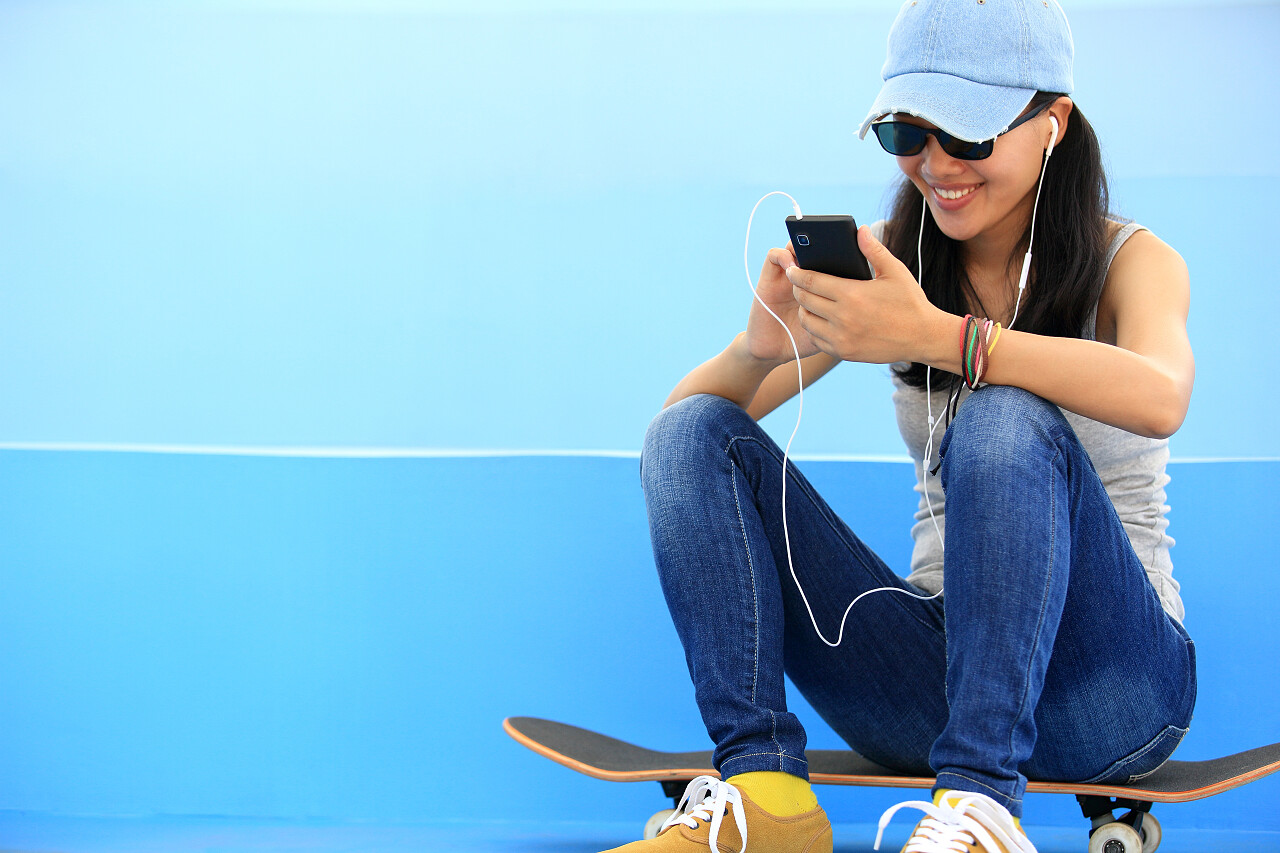 女子滑板听音乐从智能手机播放器