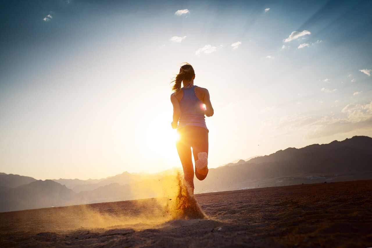 年轻的女士在日落时分在沙漠上运行努力