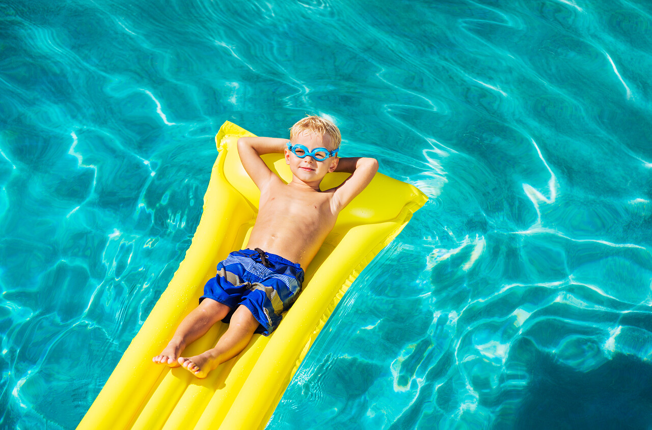小男孩躺在泳池充气筏上放松