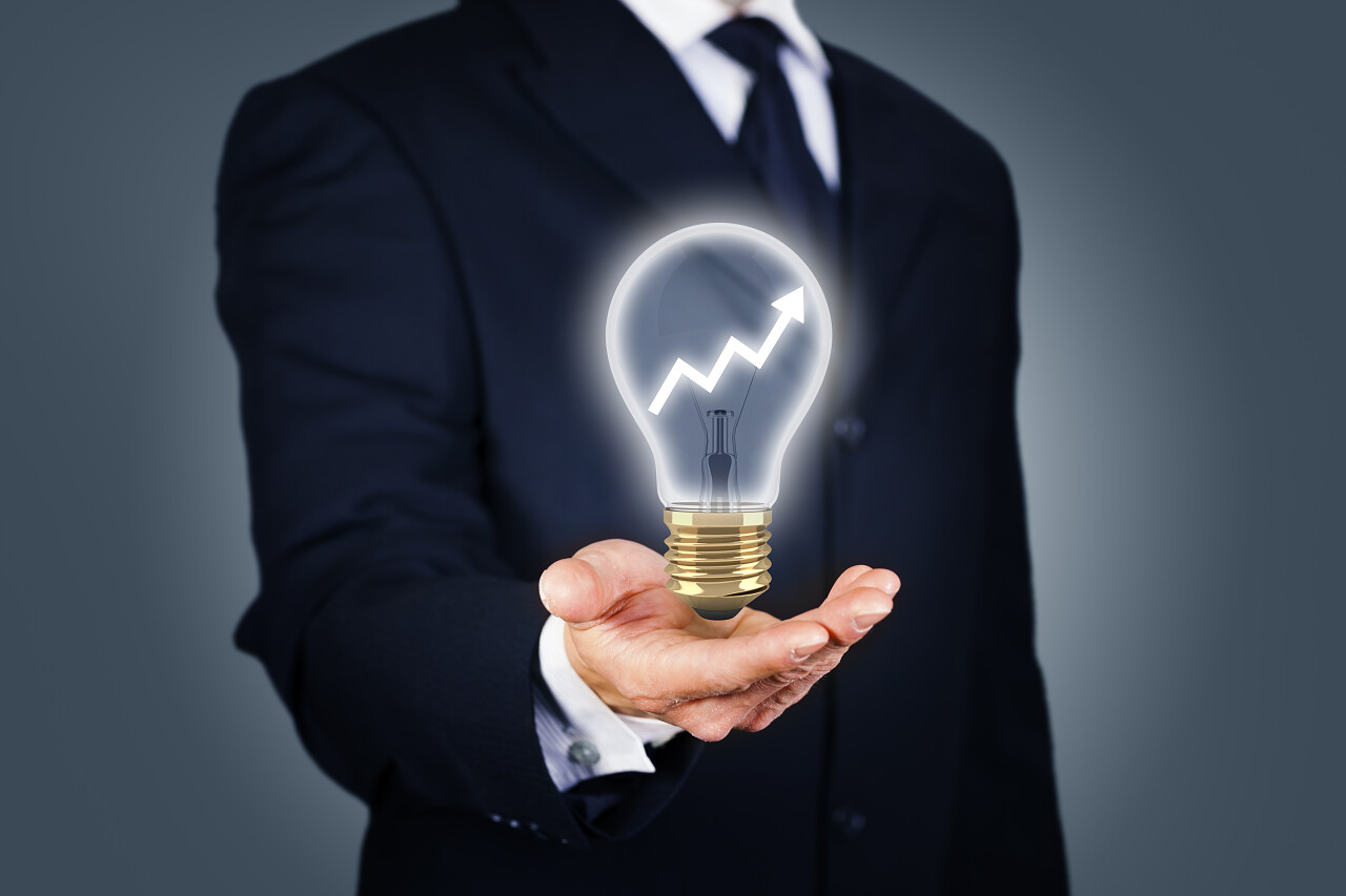 穿西装的男人手拿带有上升图的灯泡思考