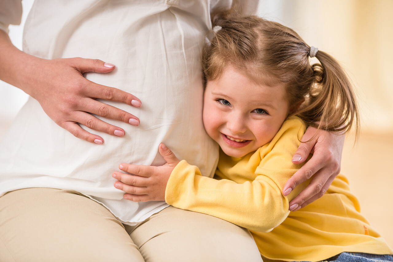 快乐的童女拥抱怀孕妈妈的肚子