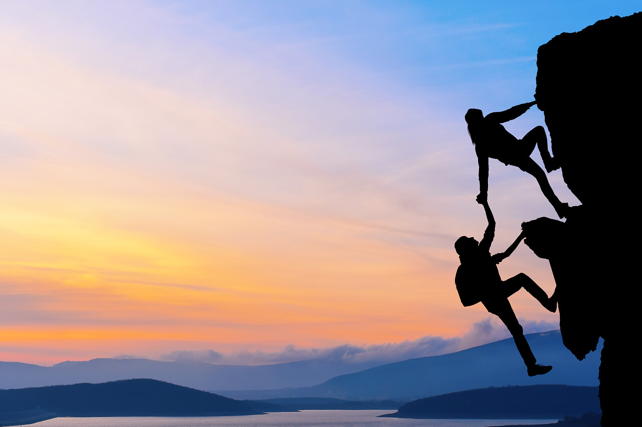 夕阳下两个男人在登山他们在登山途中相互帮助励志努力坚持不懈克服困难